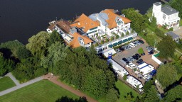 Luftaufnahme eines eleganten Hotel- und Resort-Komplexes am Ufer eines großen Sees, umgeben von dichtem Wald und gepflegten Gärten.