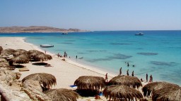 Tropischer Strand mit klarem, türkisblauem Meer und zahlreichen Strohschattenspendern.