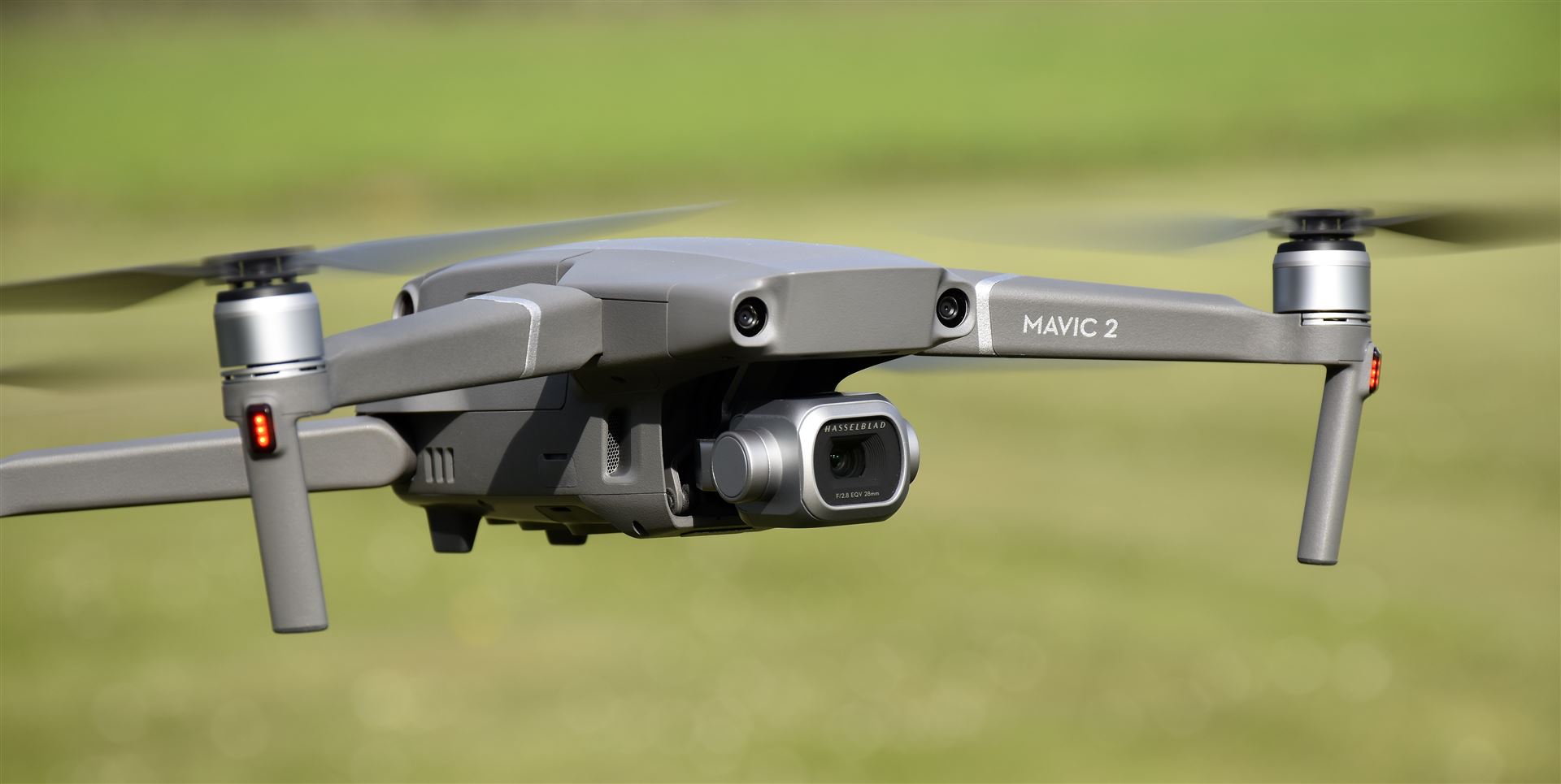 Ein grauer DJI Mavic 2 Quadcopter fliegt über einem unscharfen grünen Feld.